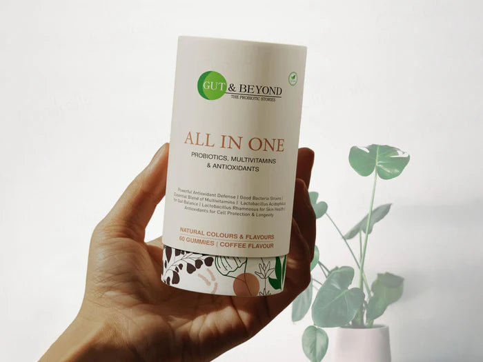 Hand holding a supplement container labeled 'Gut & Beyond All in One' with a plant in the background.